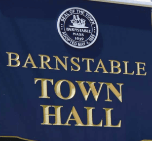 A navy blue sign with gold letters reads "Barnstable Town Hall" and features the town seal of Barnstable, Massachusetts at the top.