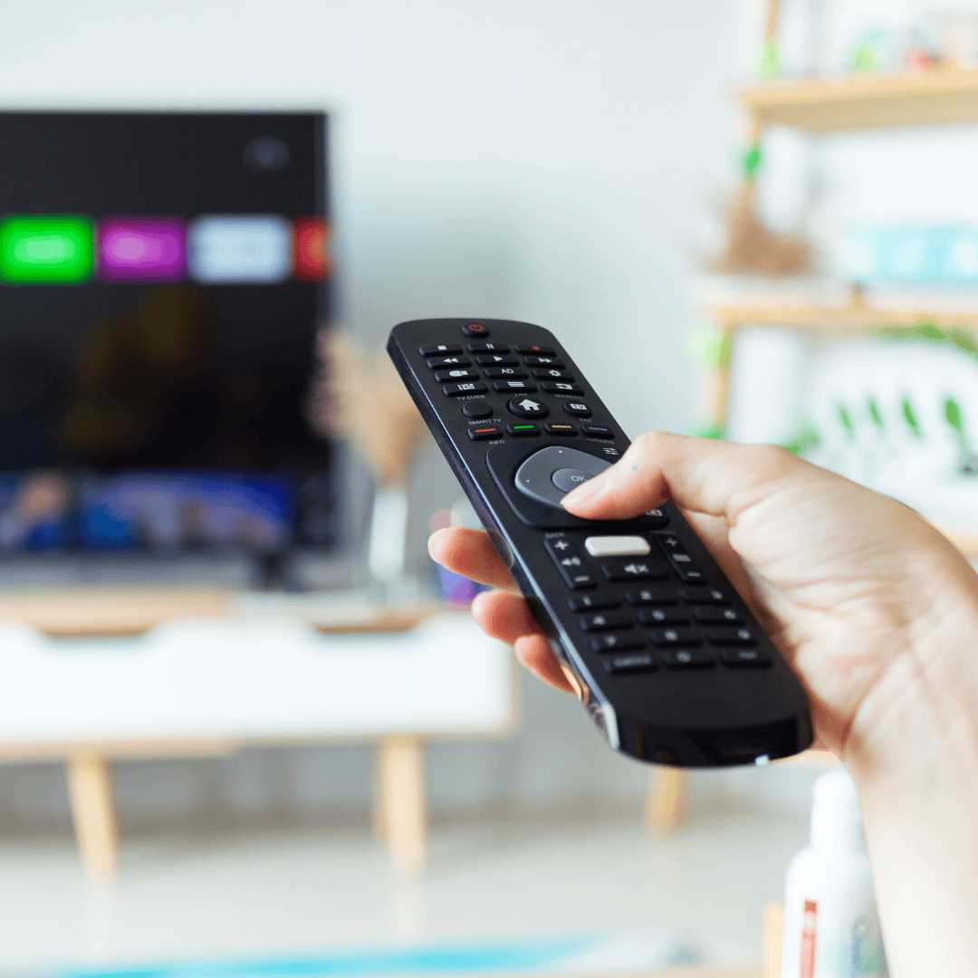 A hand holding a remote control pointed at a tv. The down arrow button is being pressed by the thumb.