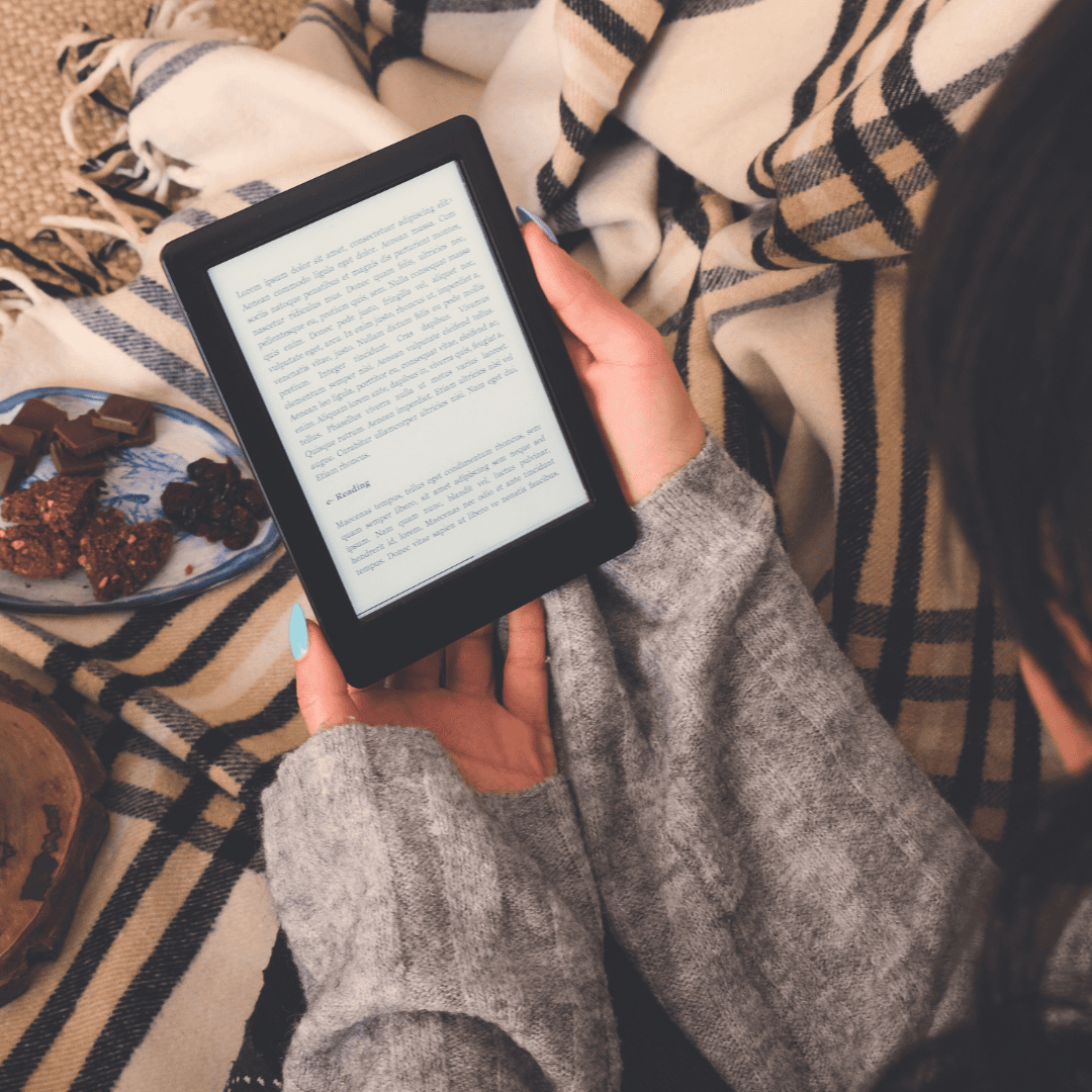 a woman under a striped blanket holding an ereader