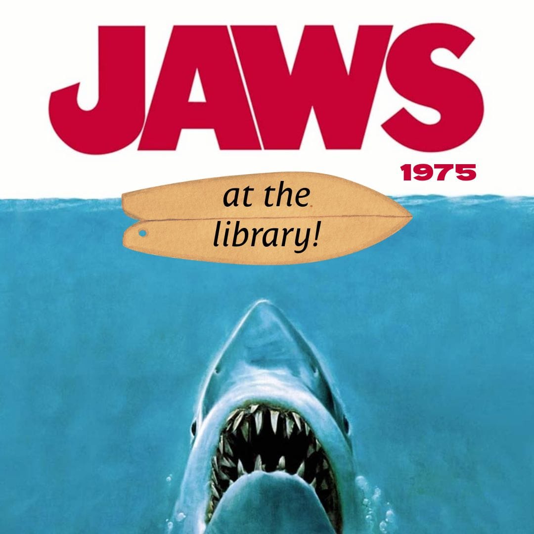 movie poster for jaws (1975) showing a shark emerging from water with text on surfboards reading "at the library!" above its head.