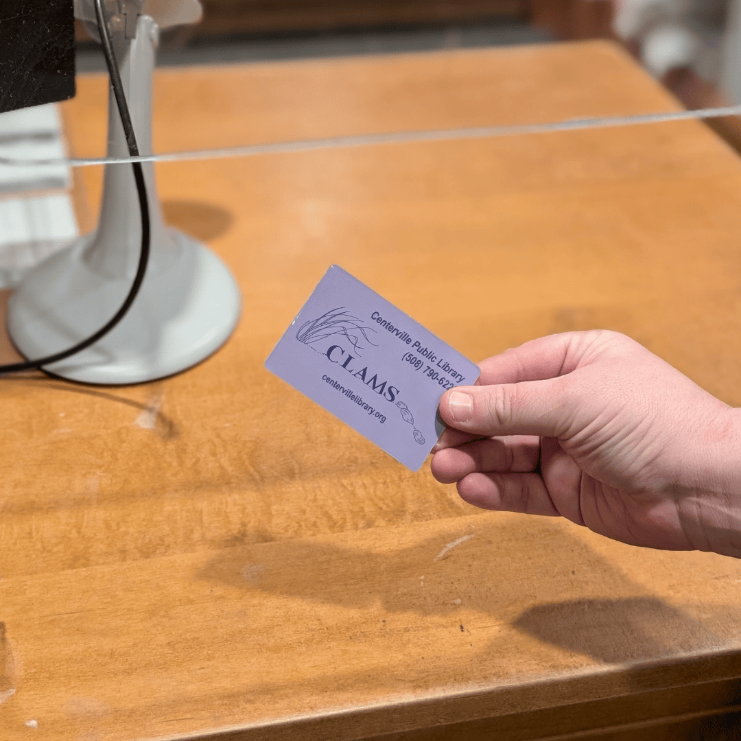 A hand holding a library card featuring the CLAMS library logo.